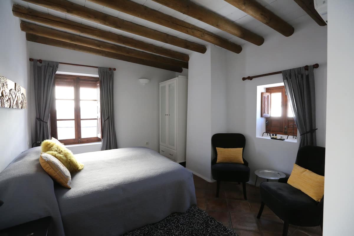 A bedroom with a bed, a chair, a small table, and a wardrobe.