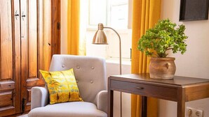 Una habitación con un sillón gris, un aparador de madera, un escritorio con planta en maceta y una lámpara.
