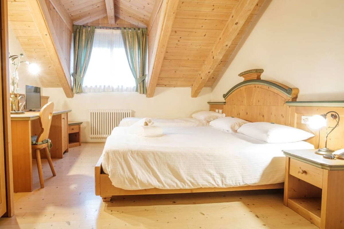 Un dormitorio con una cama de madera, un escritorio con silla, un radiador y una ventana con cortinas.