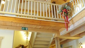 A wooden staircase with a red carpet, a white railing, and a decorative wreath. - Casa Moresc (Spiazzo)
