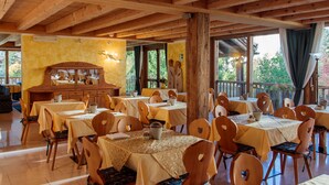 A dining area with wooden tables and chairs, a wooden buffet, and large windows with curtains. - Casa Moresc (Spiazzo)