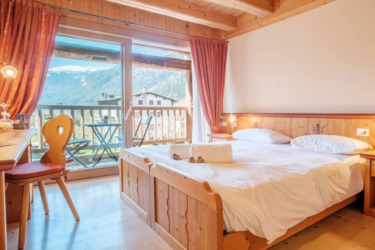 Un dormitorio de madera con una cama, mesita de noche y vistas a la montaña a través de un ventanal grande.