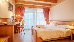 A cozy room with a wooden bed, a desk with a chair, and a window with curtains. - Casa Moresc (Spiazzo)