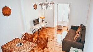 A cozy living room with a wooden floor, a sofa, a dining table with chairs, a TV, and a lamp. - Kalathos House 3 By Gt House (Lisboa ciudad)