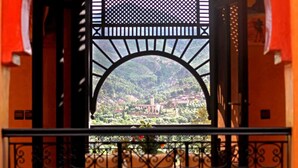 A view through a black metal archway with a decorative lattice at the top, leading to a balcony with a wrought iron railing. - Villa Tigmi (Ourika)