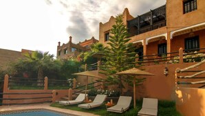 A pool area with lounge chairs, a small pool, and a building with balconies and decorative plants. - Villa Tigmi (Ourika)