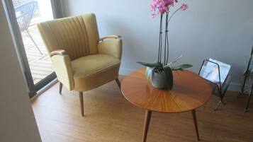Una habitación moderna con un sillón amarillo, una mesa de madera con una orquídea en maceta y una puerta de cristal que da a un espacio exterior.