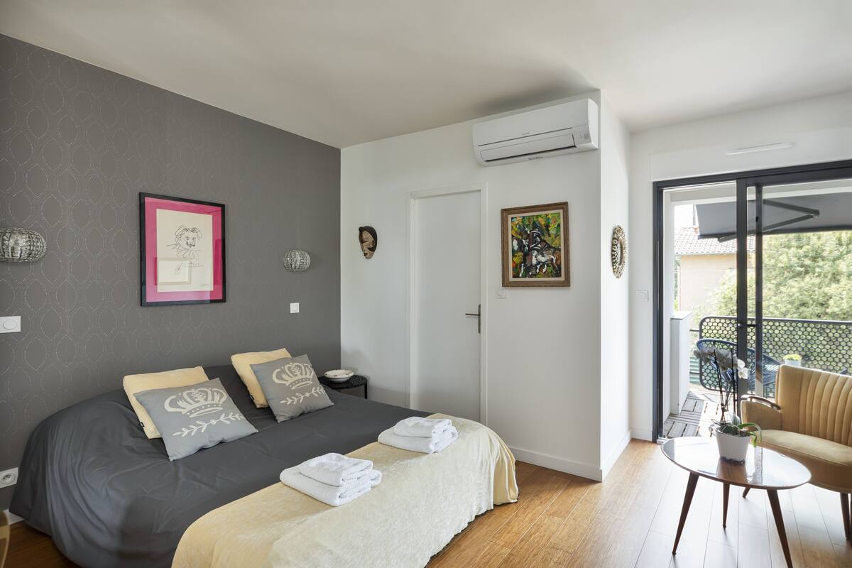 Un dormitorio con una cama grande, una mesita con una planta y un balcón con una silla.