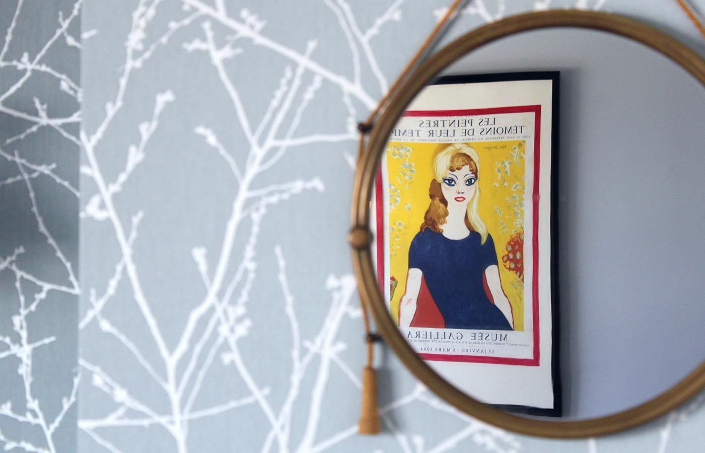 A framed artwork with a portrait on a wall with a white branch pattern.