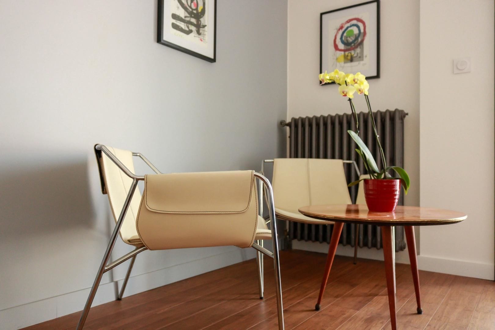 A modern room with a beige chair, a small round table with a red pot, and a radiator.