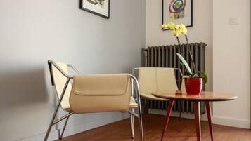 A modern room with a beige chair, a small round table with a red pot, and a radiator.