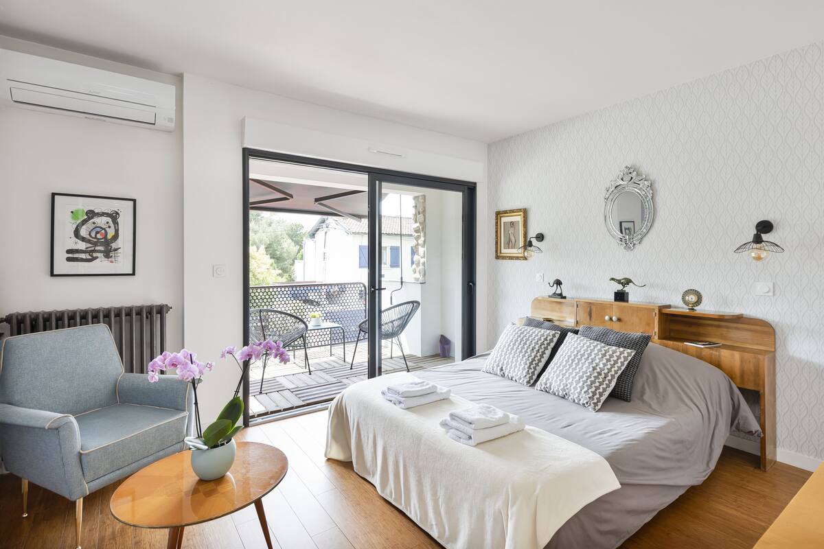 Un dormitorio moderno con cama, sofá, una mesita y un balcón con sillas.