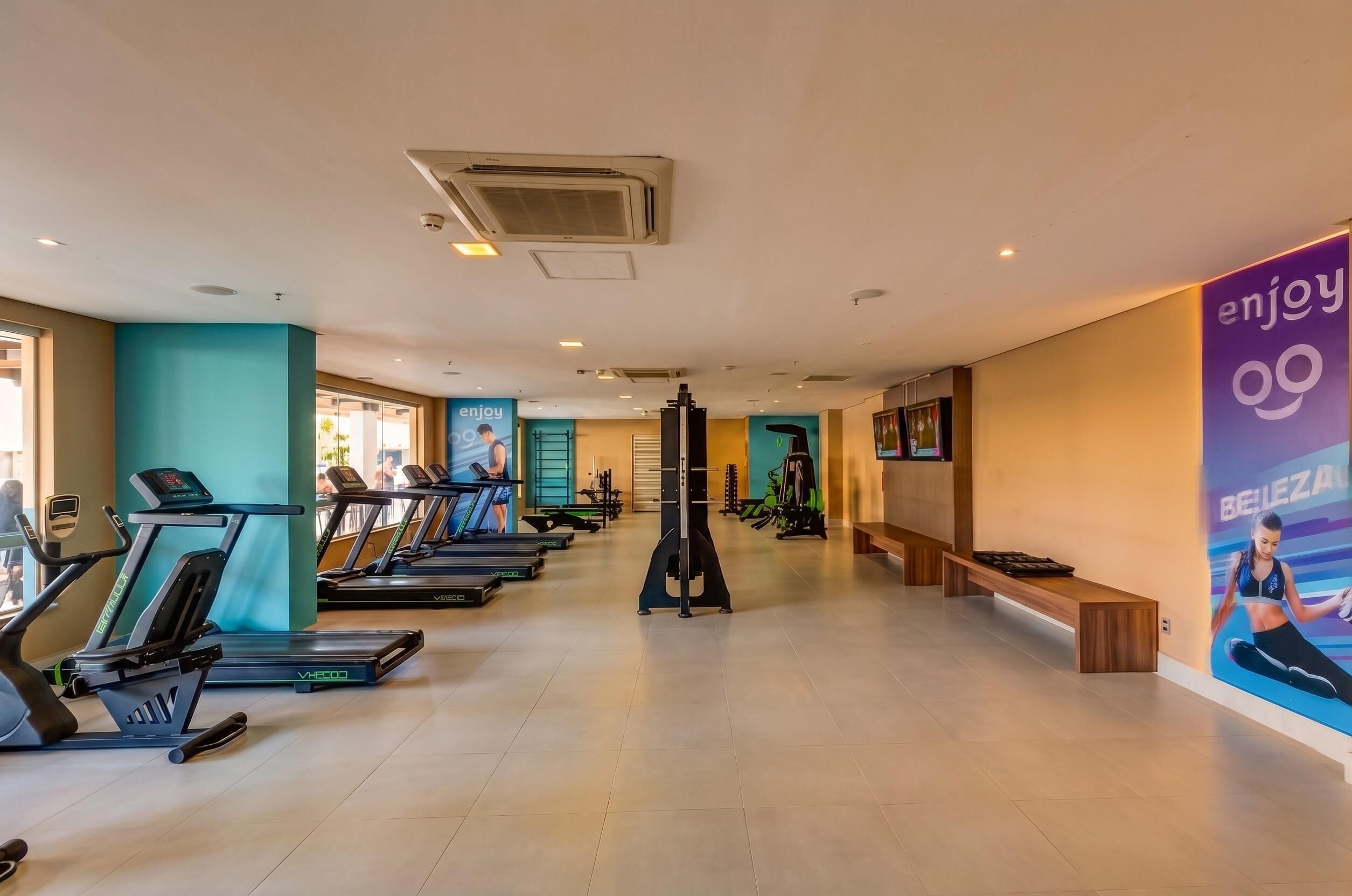 A gym with treadmills, exercise equipment, and a wall with an 'enjoy' advertisement.