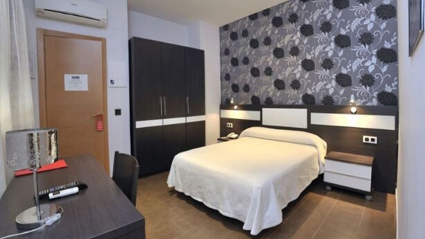 Una habitación de hotel con cama, mesitas de noche, escritorio y armario.