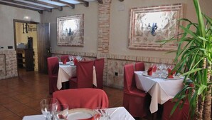 Interior de un restaurante con sillas tapizadas de rojo, manteles blancos y una planta en maceta.