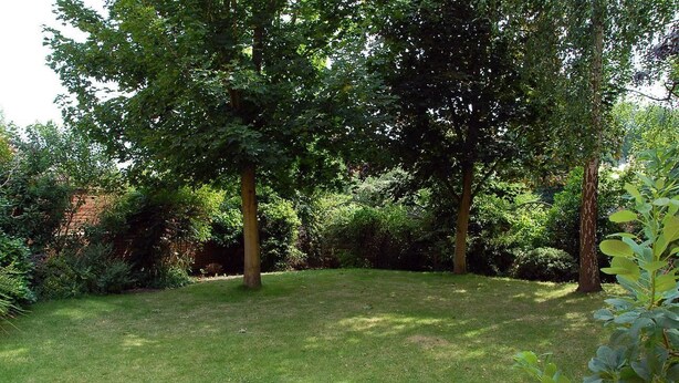 A well-maintained garden with mature trees and a grassy lawn. - Woodlands Hotel (Spalding)