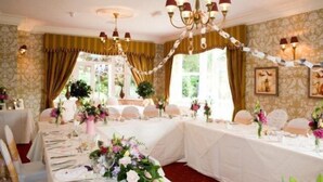 A banquet hall with tables set for a formal event, featuring chandeliers, floral centerpieces, and patterned wallpaper. - Woodlands Hotel (Spalding)