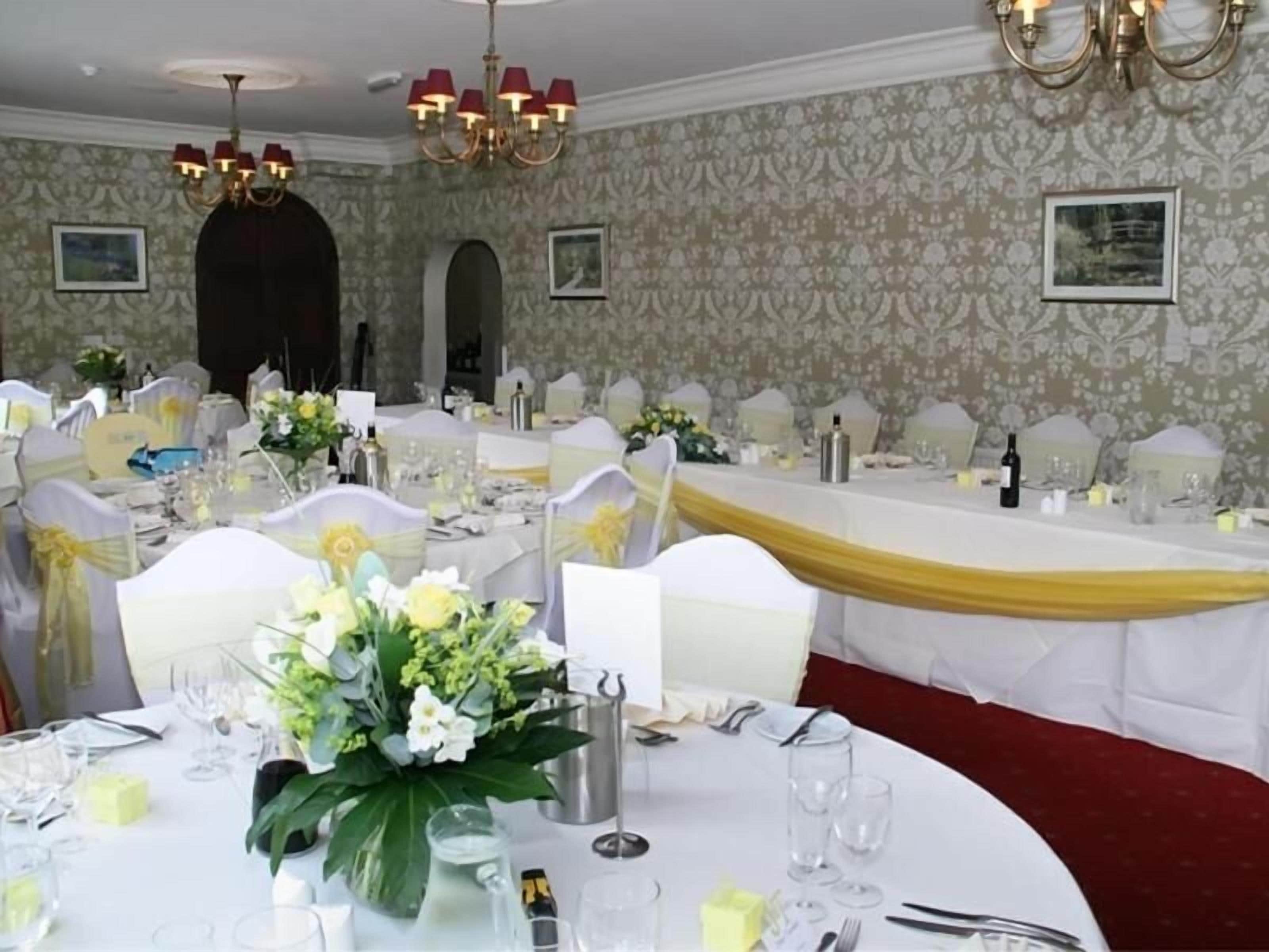 A banquet hall with round tables, white tablecloths, and chairs with yellow sashes.