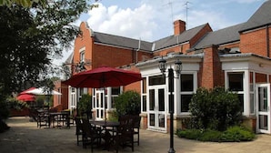 An outdoor patio area with brick buildings, red umbrellas, and outdoor seating. - Woodlands Hotel (Spalding)