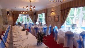 A banquet hall with long tables set for a formal event, adorned with blue sashes and white tablecloths. - Woodlands Hotel (Spalding)