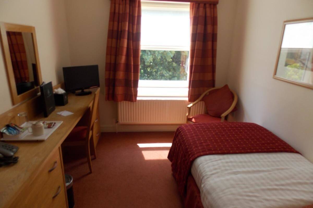 A bedroom with a bed, a desk with a computer, a chair, and a window with curtains.