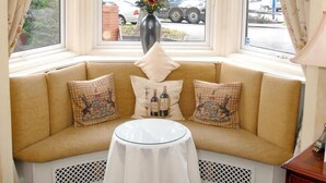 A corner seating area with a small table, floral curtains, and a view of the street outside. - Woodlands Hotel (Spalding)
