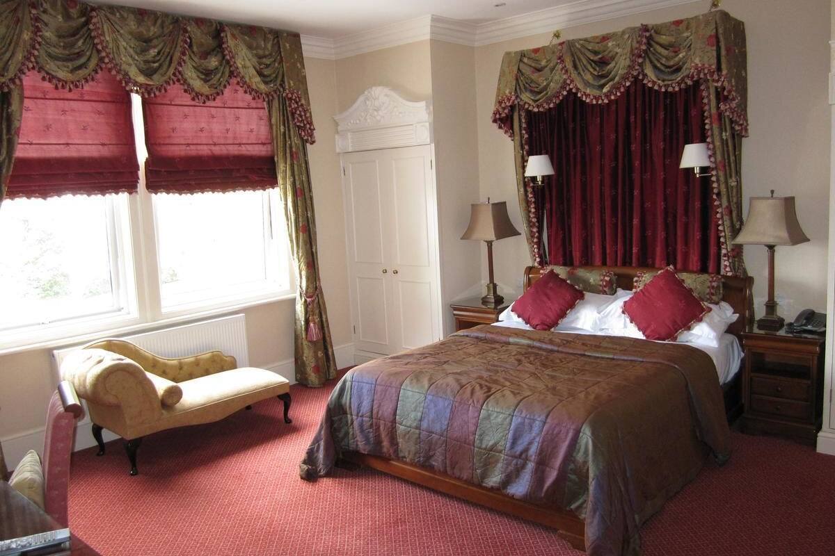 A bedroom with a large bed, two bedside tables, a nightstand, a chair, and a wardrobe.