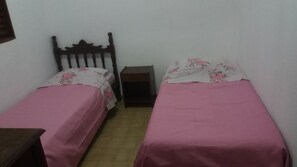 A small room with two single beds, each with a pink bedspread and floral-patterned pillows. There is a wooden headboard on one bed and a small bedside table between the beds. - Casa Mineira (Capitólio)