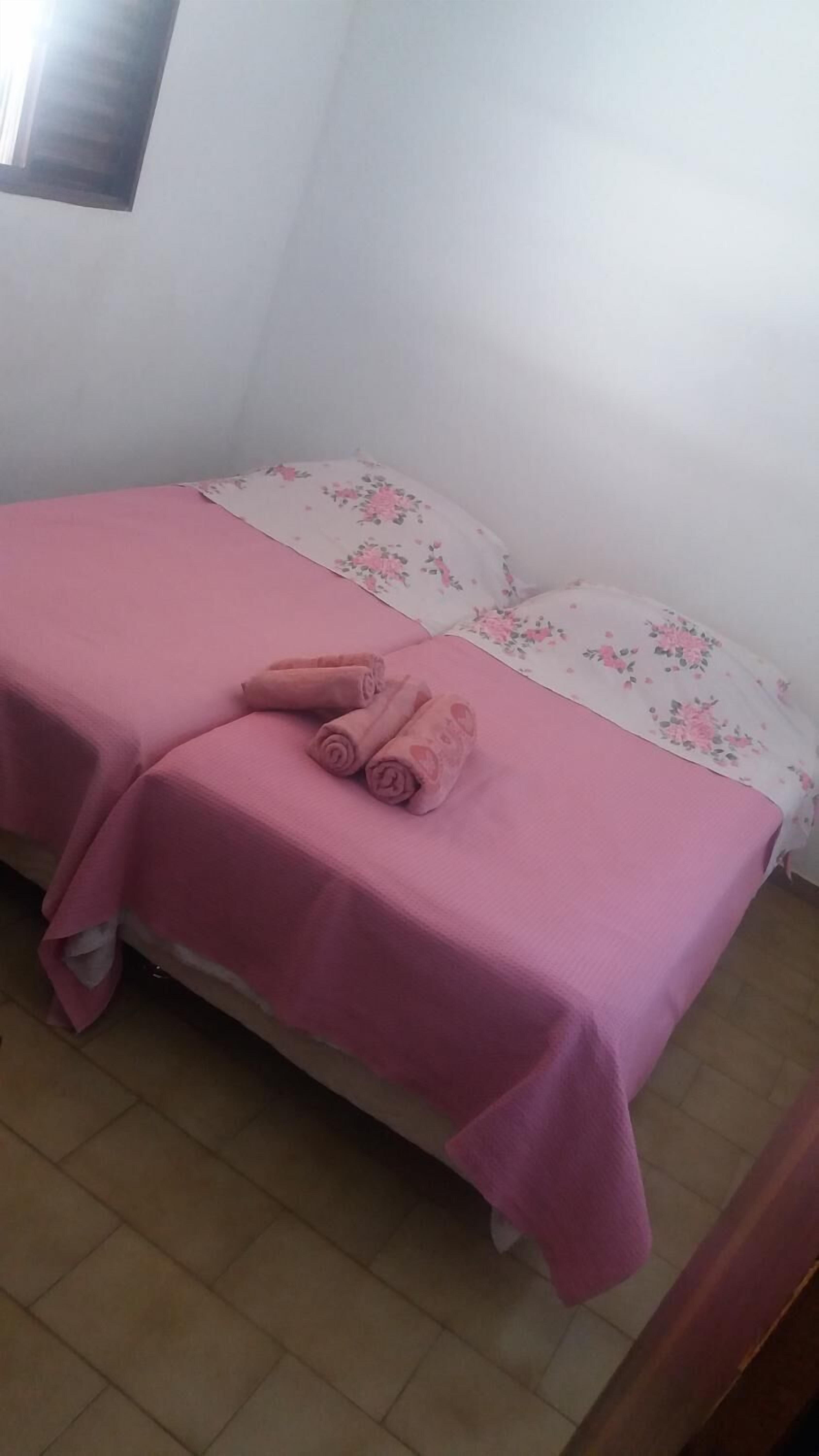 A small, single-bed room with pink bedding and floral-patterned pillows.