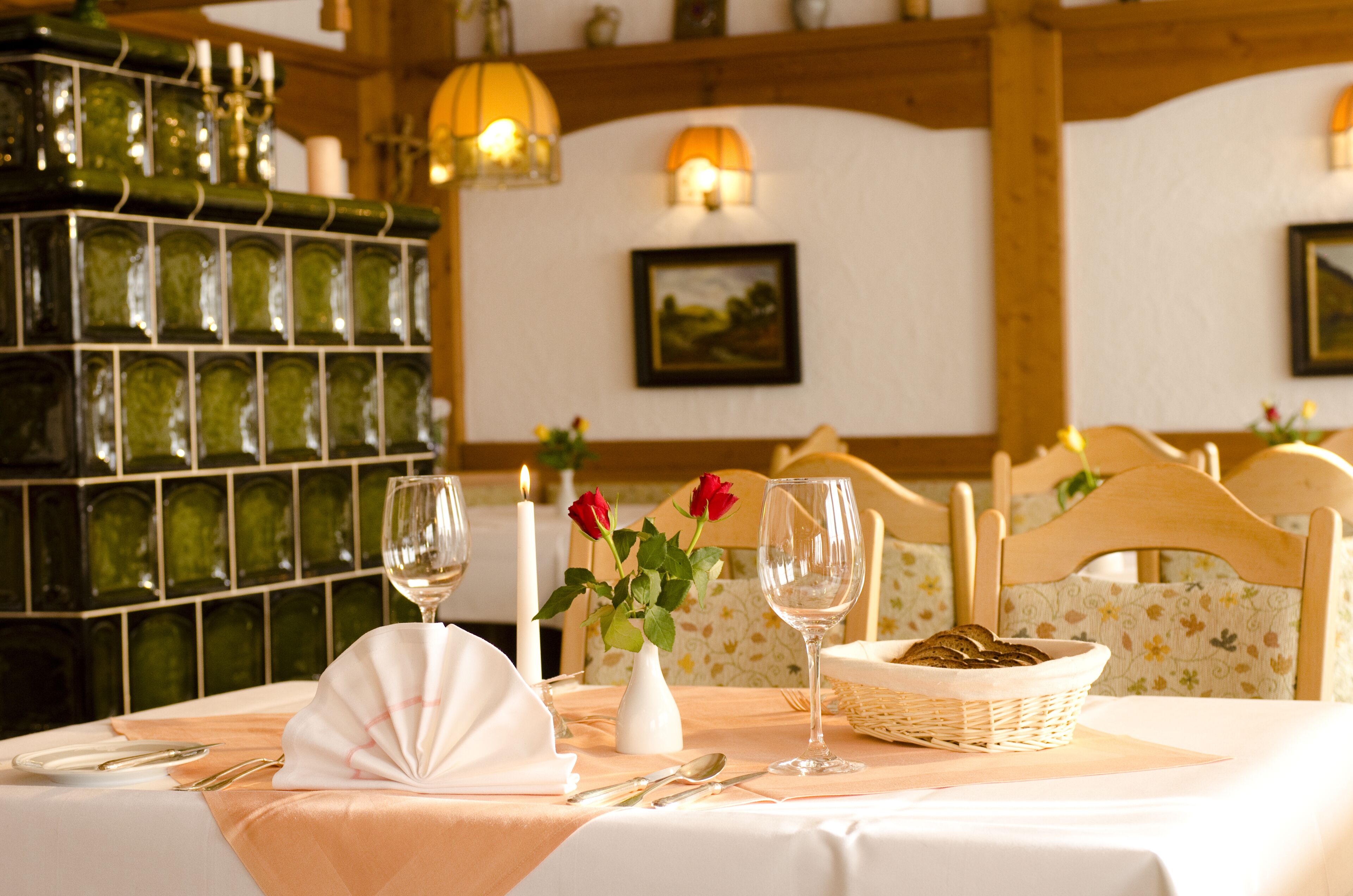 A dining table set with a white tablecloth, a vase with red roses, and a basket of bread.