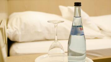 A bottle of water and an empty wine glass on a white plate on a bedside table in a hotel room.