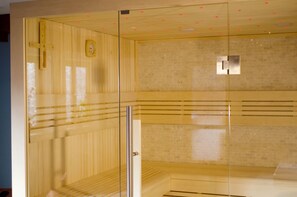 A sauna room with wooden paneling, a glass door, and a tiled wall. - Hotel Mutzel (Schluchsee)
