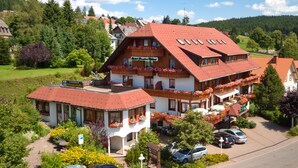 A large, multi-story hotel with a red-tiled roof, balconies with flower boxes, and a sign indicating it is a restaurant. - Hotel Mutzel (Schluchsee)