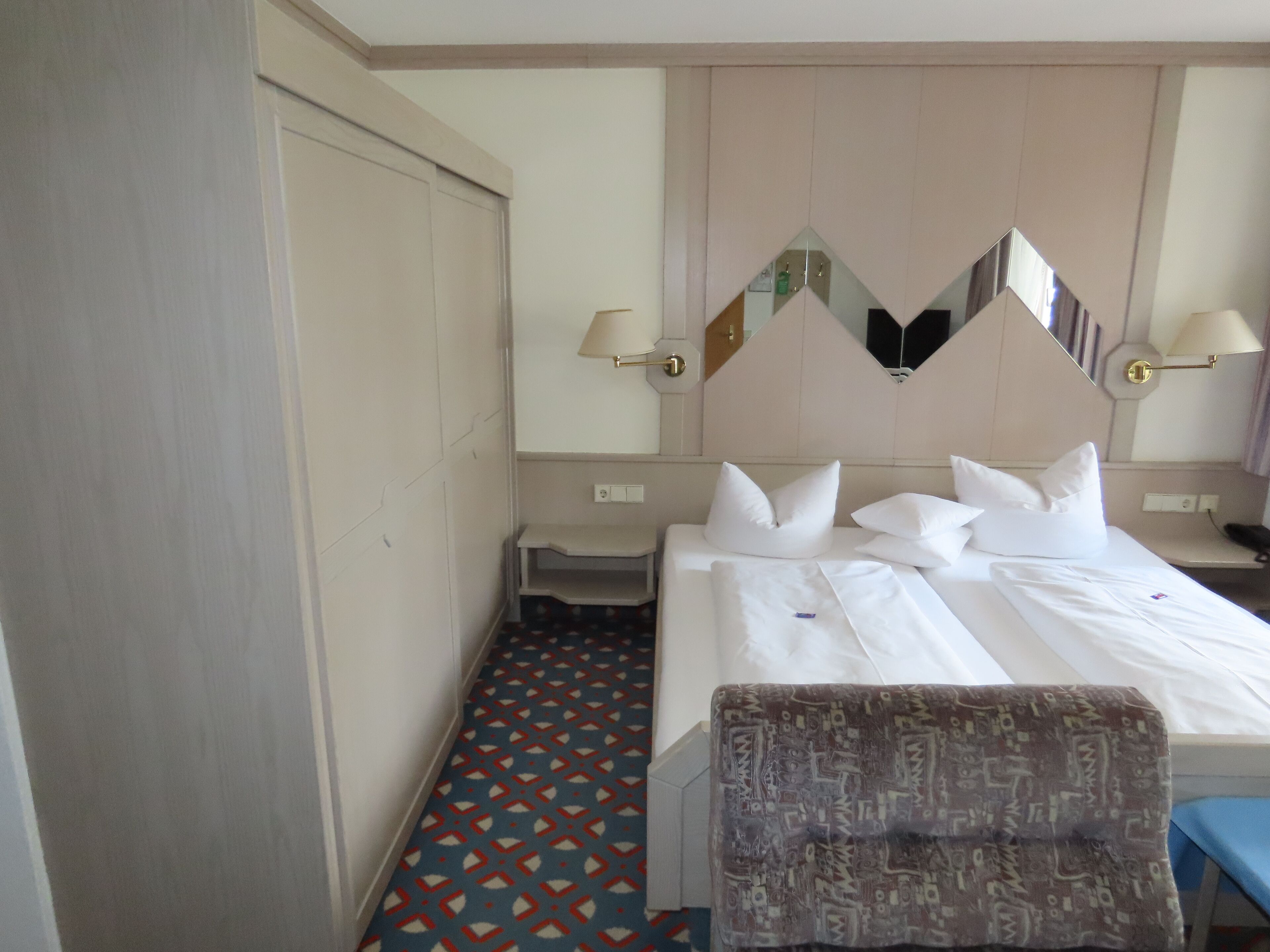 Une chambre d’hôtel avec un lit, des tables de chevet, un miroir et un sol à motifs.