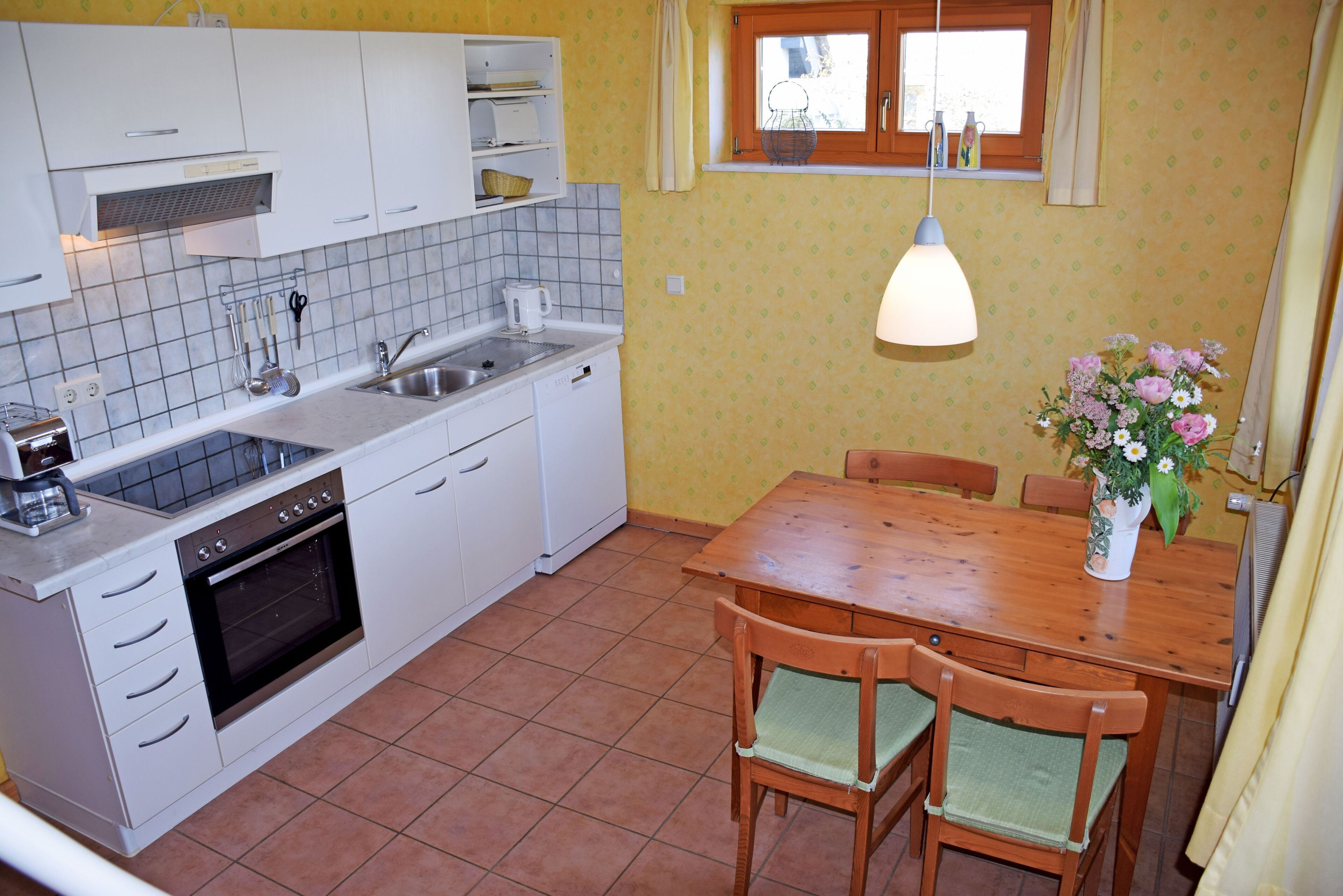 A kitchen with white cabinets, a tiled backsplash, a wooden dining table, and a vase with flowers.