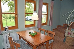 A dining area with a wooden table, chairs, and a view of a car and trees through large windows.