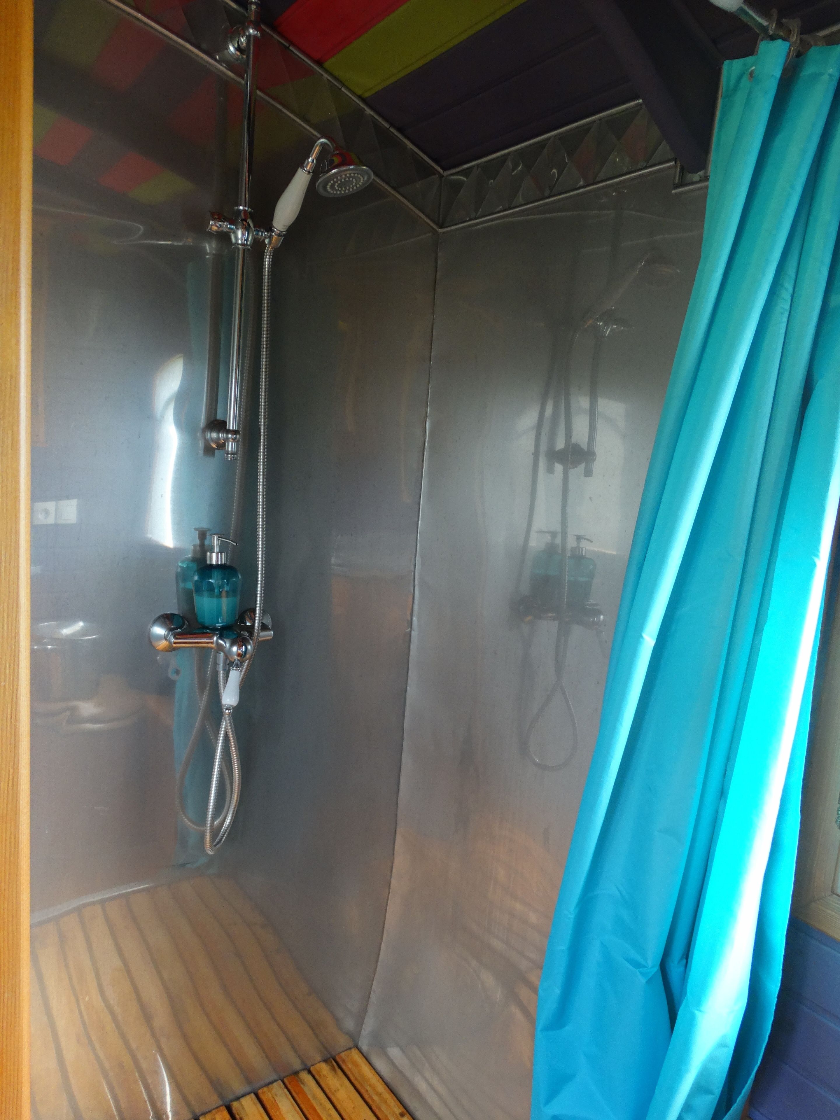 Een douche met een handdouche, een douchecabine met glazen wanden en een blauw douchegordijn.