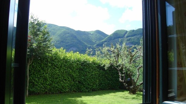A window with a view of a lush green garden and rolling hills in the distance.