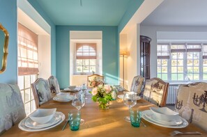 A dining room with a wooden table set for four, chairs with ornate backs, and a vase of flowers.