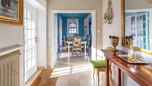 A hallway with a dining area in the background, a chandelier, and a mirror. - Homerez - Villa in Roscoff, sea view (Roscoff)
