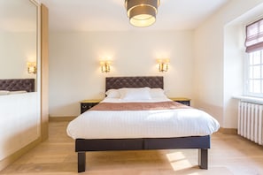 A bedroom with a large bed, two bedside tables, a mirror, and a window with curtains.