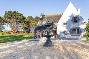 A large, white building with a prominent triangular roof and a stone fountain in the foreground. - Homerez - Villa in Roscoff, sea view (Roscoff)