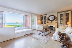 Amplia sala de estar con un ventanal que da al mar, una chimenea y una estatua.