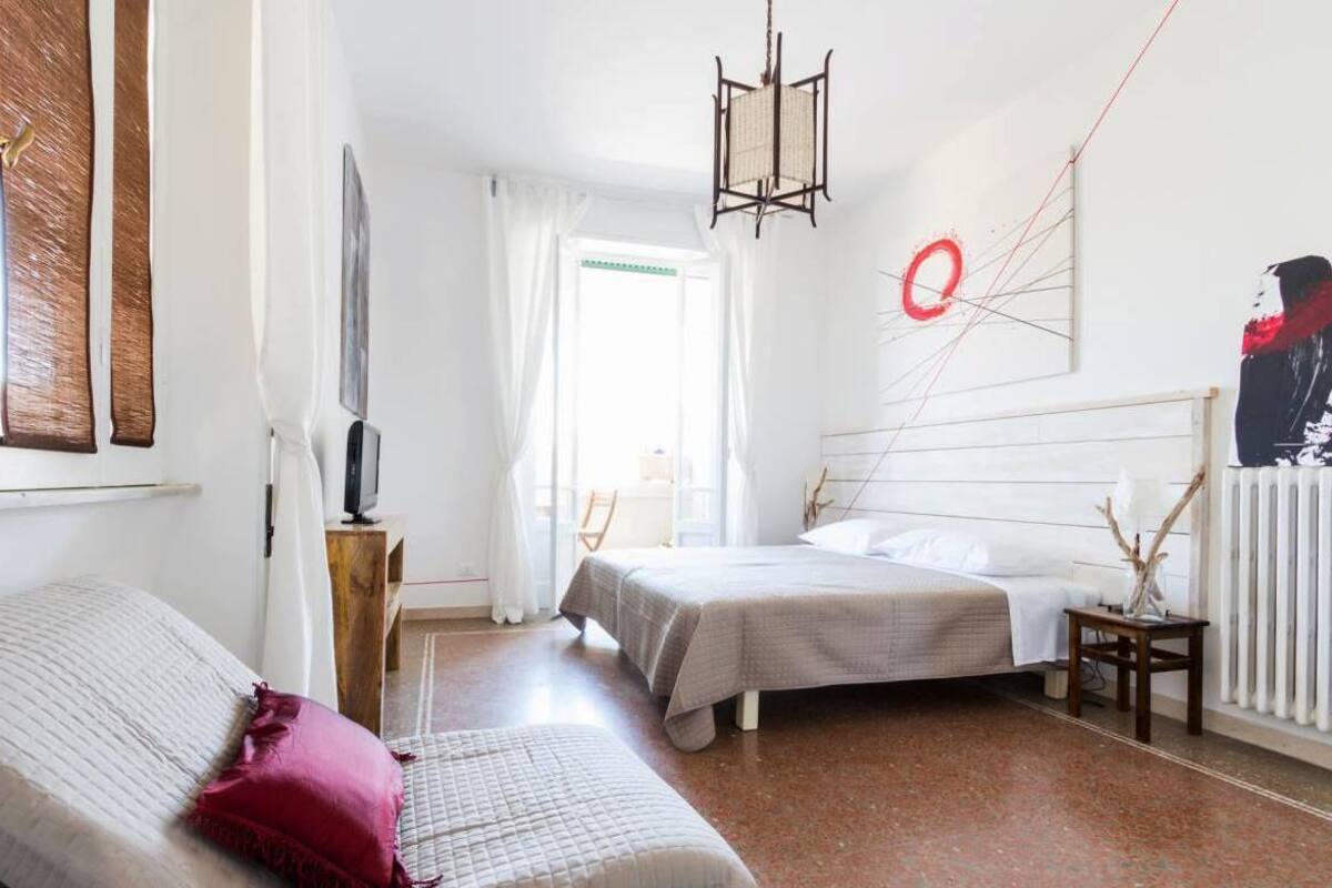 Une chambre avec deux lits, une télévision, une fenêtre avec des rideaux et un mur orné d’un motif circulaire rouge.