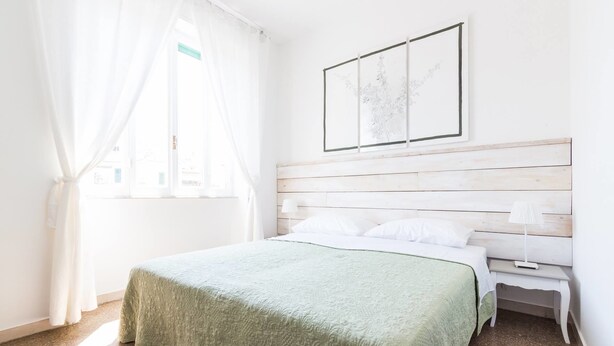 A bedroom with a bed, a nightstand, a window with curtains, and a wall-mounted picture. - B&B In White (Rome)