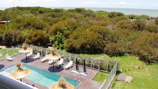 Area piscina con lettini e ombrelloni, immersa nel verde e affacciata su un corpo d'acqua.