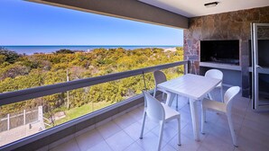Un balcone con tavolo e sedie, un muro in pietra e vista sul mare e sul verde.