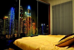 A bedroom with a large window overlooking a cityscape at night.