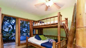 Une chambre avec un lit en bambou, un ventilateur de plafond et une vue sur l’extérieur.