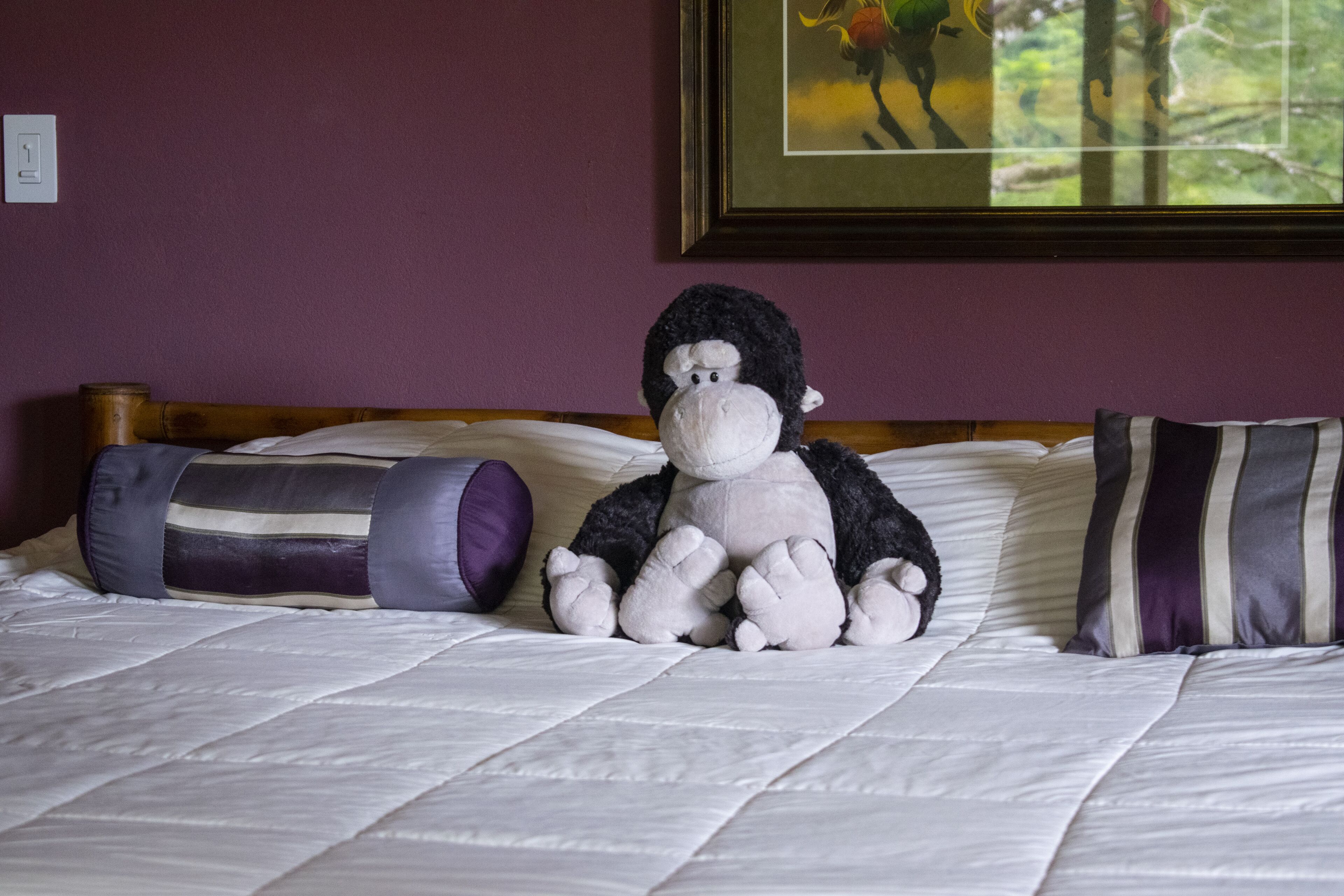 Un lit avec un doudou, un oreiller à rayures et un tableau encadré accroché au mur.